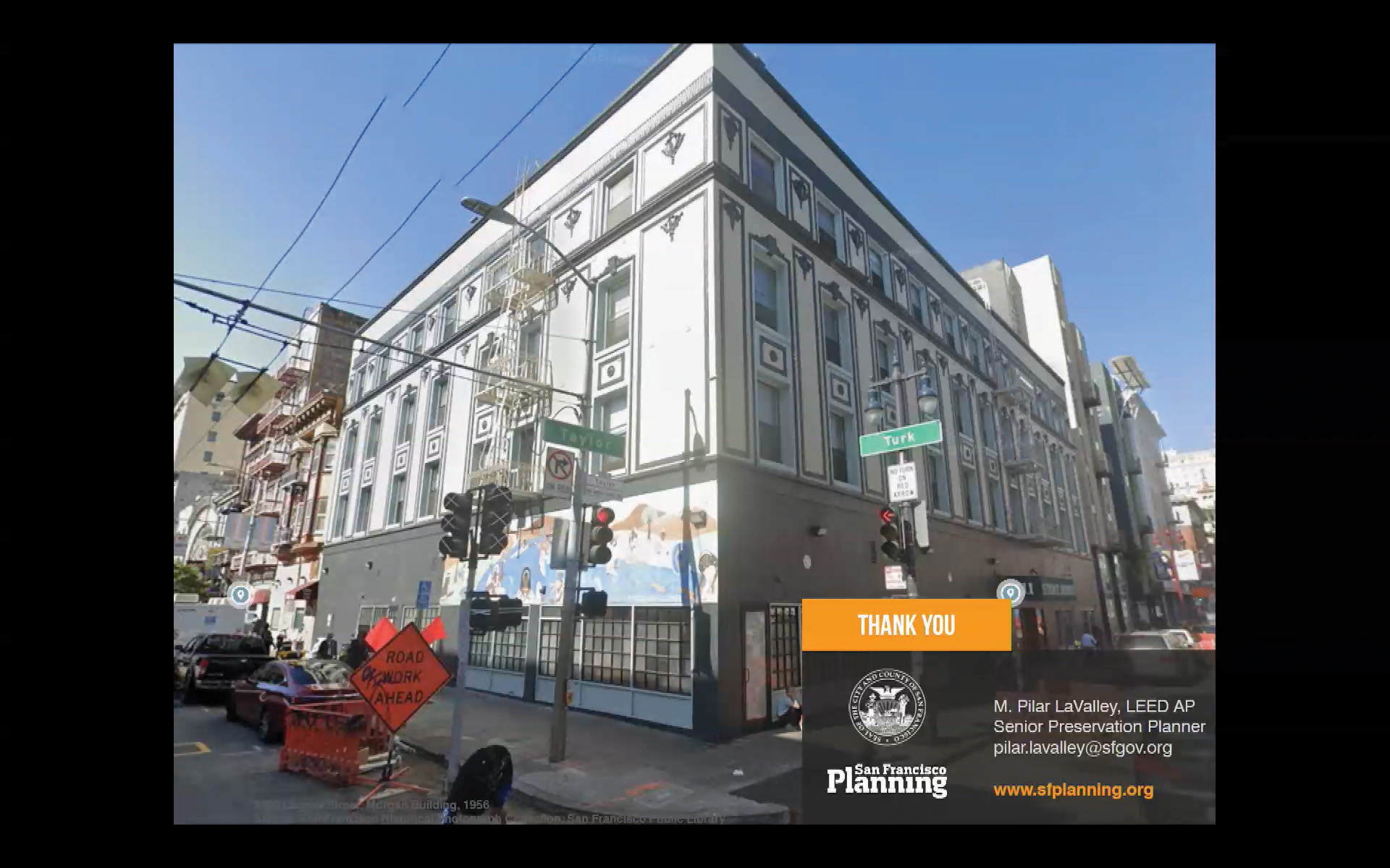 A modern daytime view of the four-story corner building at Turk and Taylor streets in San Francisco’s Tenderloin neighborhood, the former site of Gene Compton’s Cafeteria, showing its ornate façade, street murals, and surrounding intersection. Photo: Screenshot of the San Francisco Historic Preservation Commission via SFGov TV