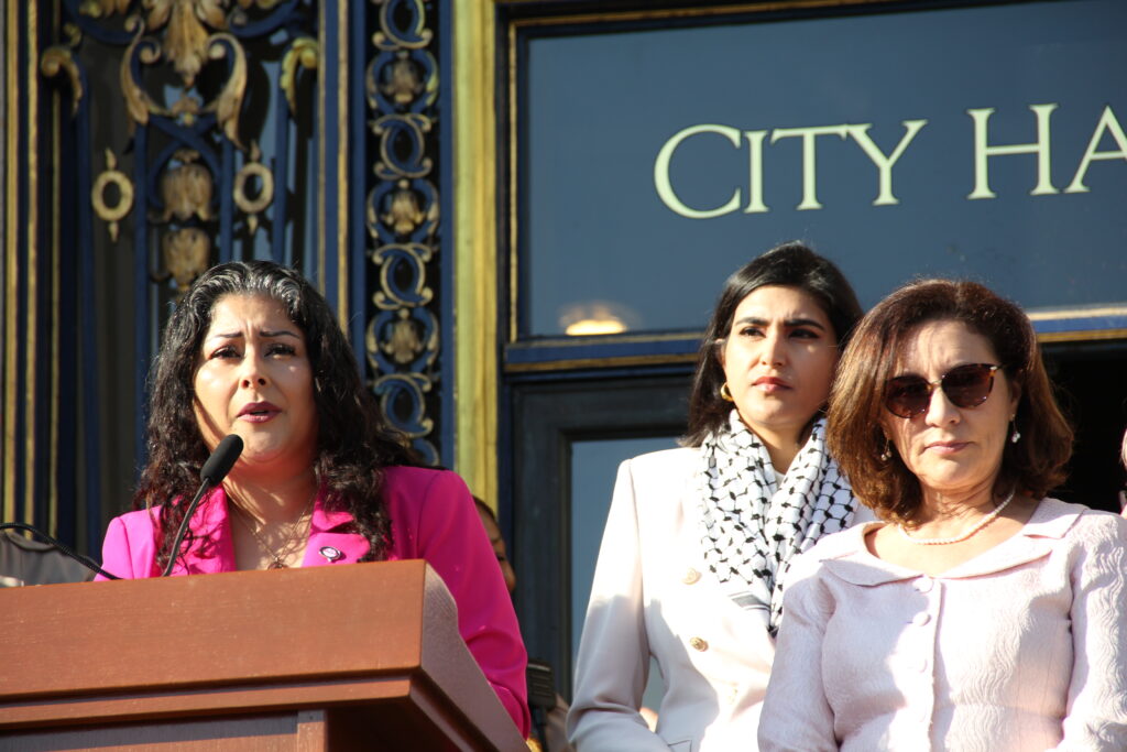 Dr. Diana Aroche stands at a podium speaking during a reproductive rights rally on the steps of San Francisco City Hall, with city officials standing behind her, marking the 53rd anniversary of Roe v. Wade. Photo: Courtesy of the San Francisco Department on the Status of Women