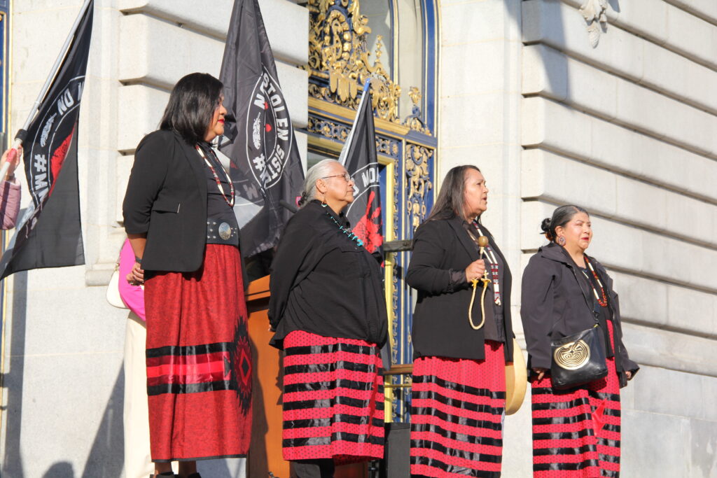 Four members of the Red Lightning Woman Power Singers stand in traditional black and red regalia performing Indigenous opening songs on the steps of San Francisco City Hall during a reproductive rights rally marking the 53rd anniversary of Roe v. Wade.