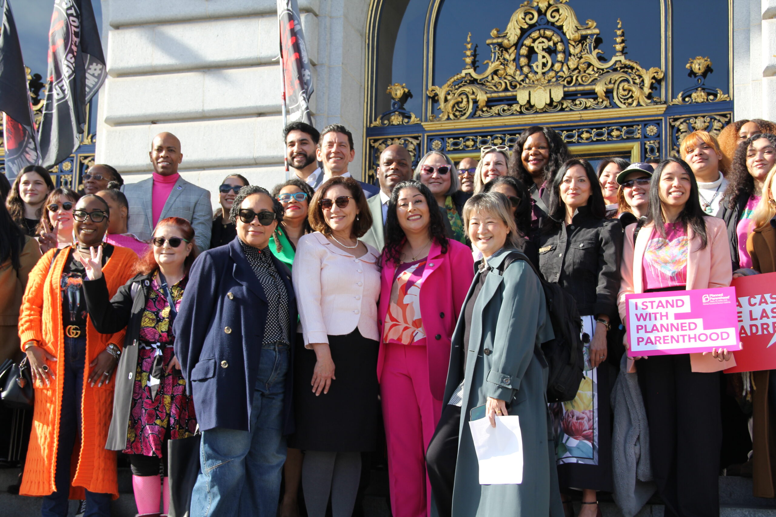 A large group of San Francisco reproductive rights advocates and city officials pose together on the steps of San Francisco City Hall during a rally marking the 53rd anniversary of Roe v. Wade, with signs supporting Planned Parenthood visible. Photo: Courtesy of the San Francisco Department on the Status of Women