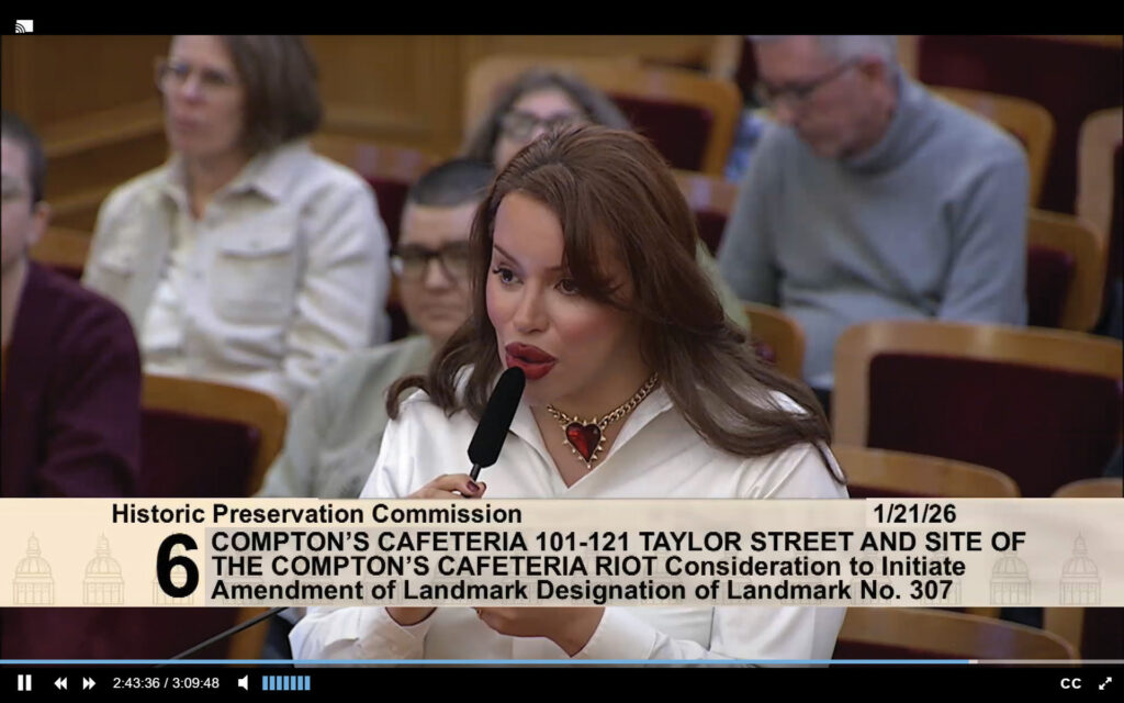 Santana Tapia, wearing a white blouse and heart-shaped necklace, speaks into a microphone while testifying before the San Francisco Historic Preservation Commission at City Hall in support of expanding landmark protections for the Compton’s Cafeteria riots site. Photo: Screenshot of the San Francisco Historic Preservation Commission via SFGov TV
