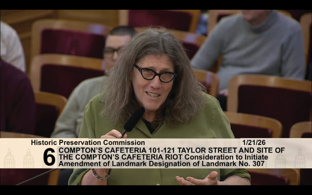 Dr. Susan Stryker, a transgender historian wearing glasses and a green blouse, speaks into a microphone while addressing the San Francisco Historic Preservation Commission at City Hall about the difficulty of determining the exact date of the 1966 Compton’s Cafeteria riots. Photo: Screenshot of the San Francisco Historic Preservation Commission via SFGov TV