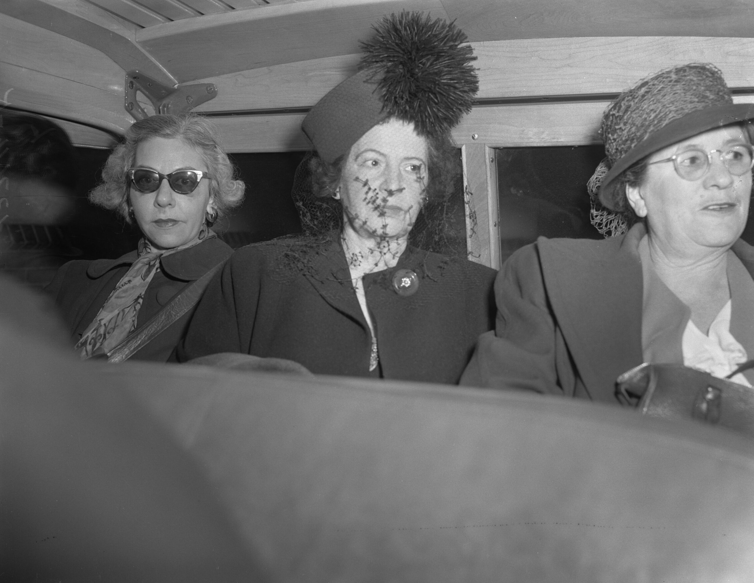 Inez Burns (center), a San Francisco abortion provider, sits in a vehicle with two of her staff as they are transported to jail in 1948, all wearing hats and coats.